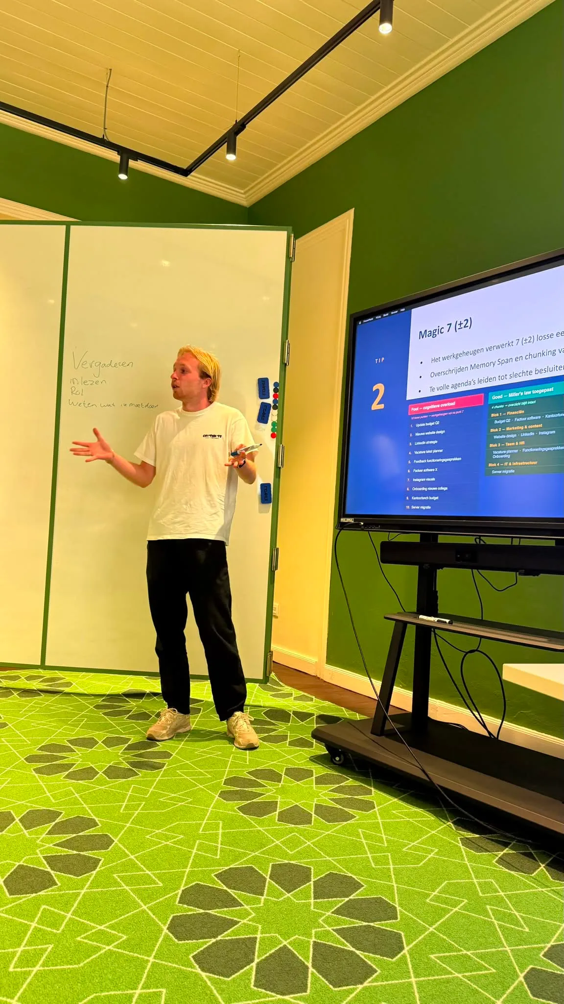 Jesse geeft een training: hij staat voor een whiteboard en een scherm met een groep